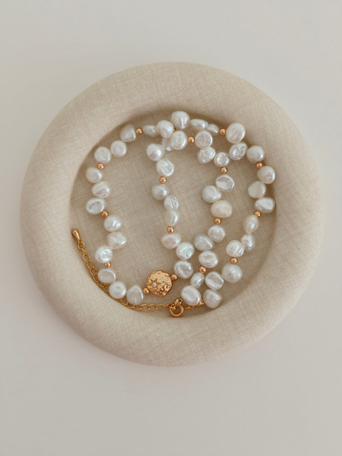 Close view of irregular baroque pearls with gold-tone spacers and an extension chain on a beige fabric display