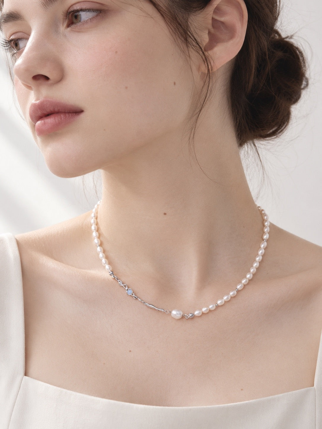 Liquid Metal pearl necklace in platinum silver worn with a cream top, showing pearl and sculpted accents at the neckline