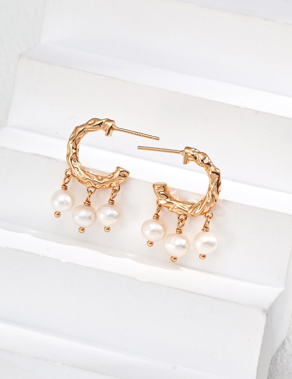 Pair of textured pearl hoop earrings in vintage gold, with three pearl drops on each hoop, displayed on a white block