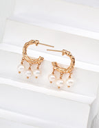 Pair of textured pearl hoop earrings in vintage gold, with three pearl drops on each hoop, displayed on a white block