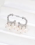 Pair of textured pearl hoop earrings in platinum silver, with three pearl drops on each hoop, displayed on a white block