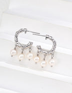 Pair of textured pearl hoop earrings in platinum silver, with three pearl drops on each hoop, displayed on a white block