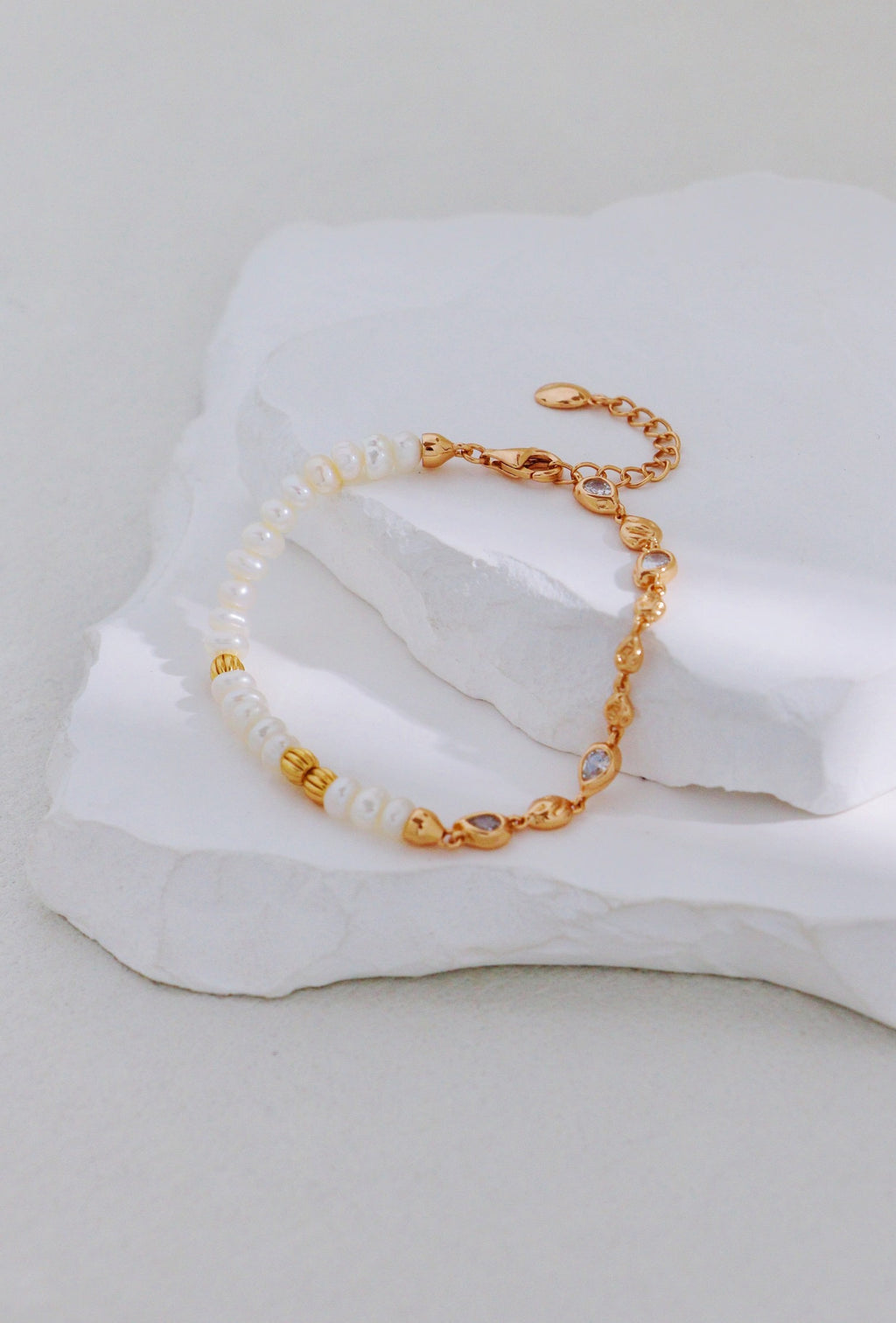 Vintage gold bracelet with pearls on one side and linked accents on the other, arranged on a white stone display