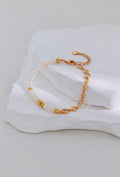 Vintage gold bracelet with pearls on one side and linked accents on the other, arranged on a white stone display