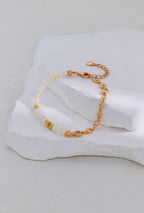 Vintage gold bracelet with pearls on one side and linked accents on the other, arranged on a white stone display