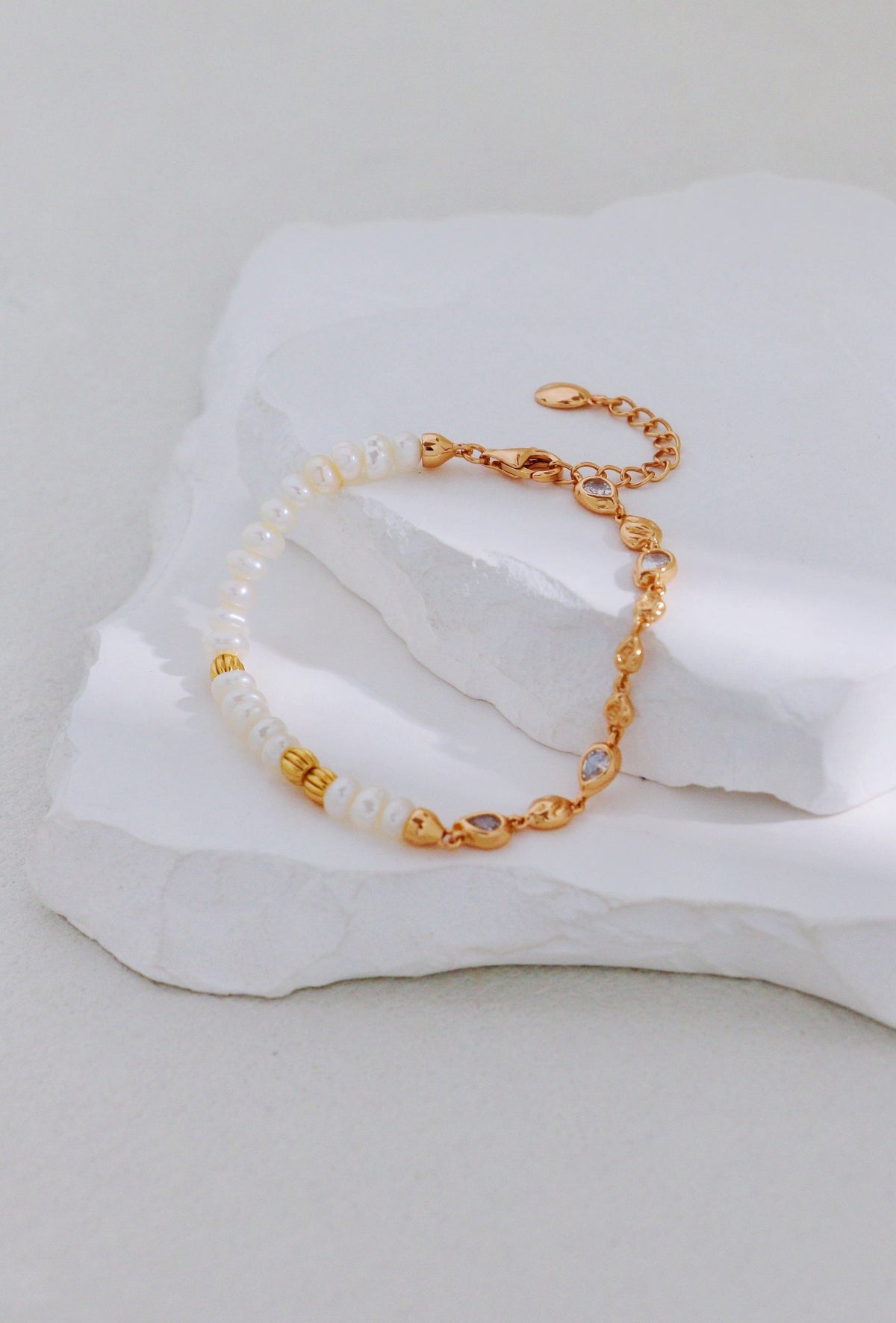Vintage gold bracelet with pearls on one side and linked accents on the other, arranged on a white stone display