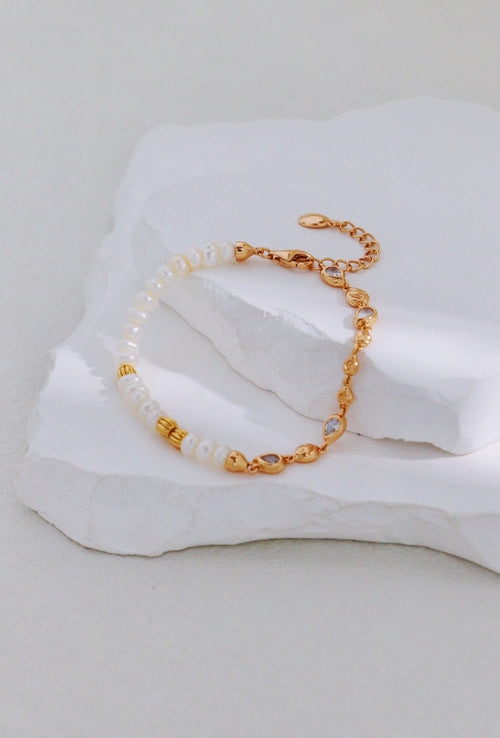 Vintage gold bracelet with pearls on one side and linked accents on the other, arranged on a white stone display