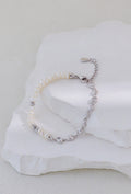 Platinum silver bracelet with pearls on one side and linked accents on the other, arranged on a white stone display