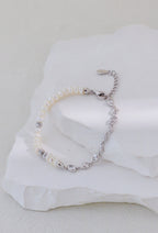Platinum silver bracelet with pearls on one side and linked accents on the other, arranged on a white stone display