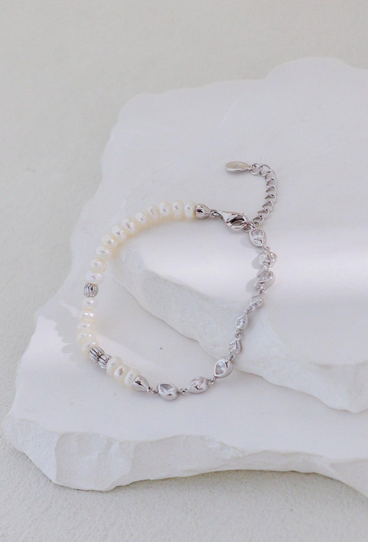 Platinum silver bracelet with pearls on one side and linked accents on the other, arranged on a white stone display