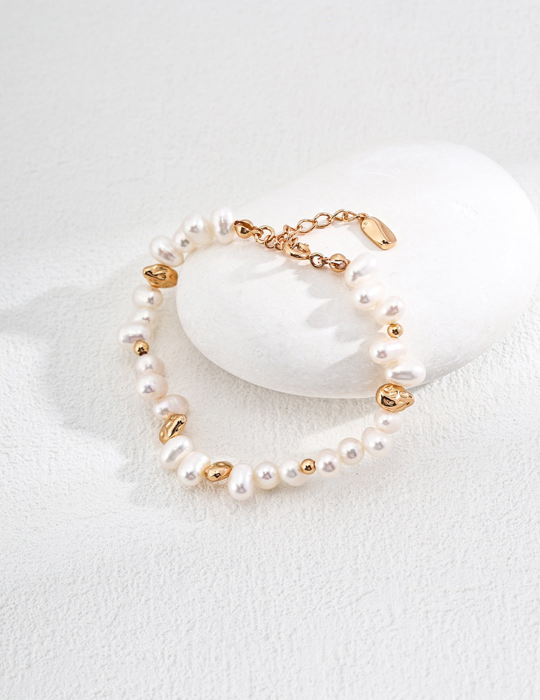 Baroque pearl bracelet in vintage gold resting against a white stone, showing pearl shapes, gold accents and the extension chain