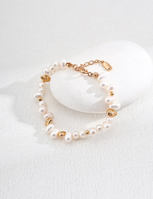 Baroque pearl bracelet in vintage gold resting against a white stone, showing pearl shapes, gold accents and the extension chain