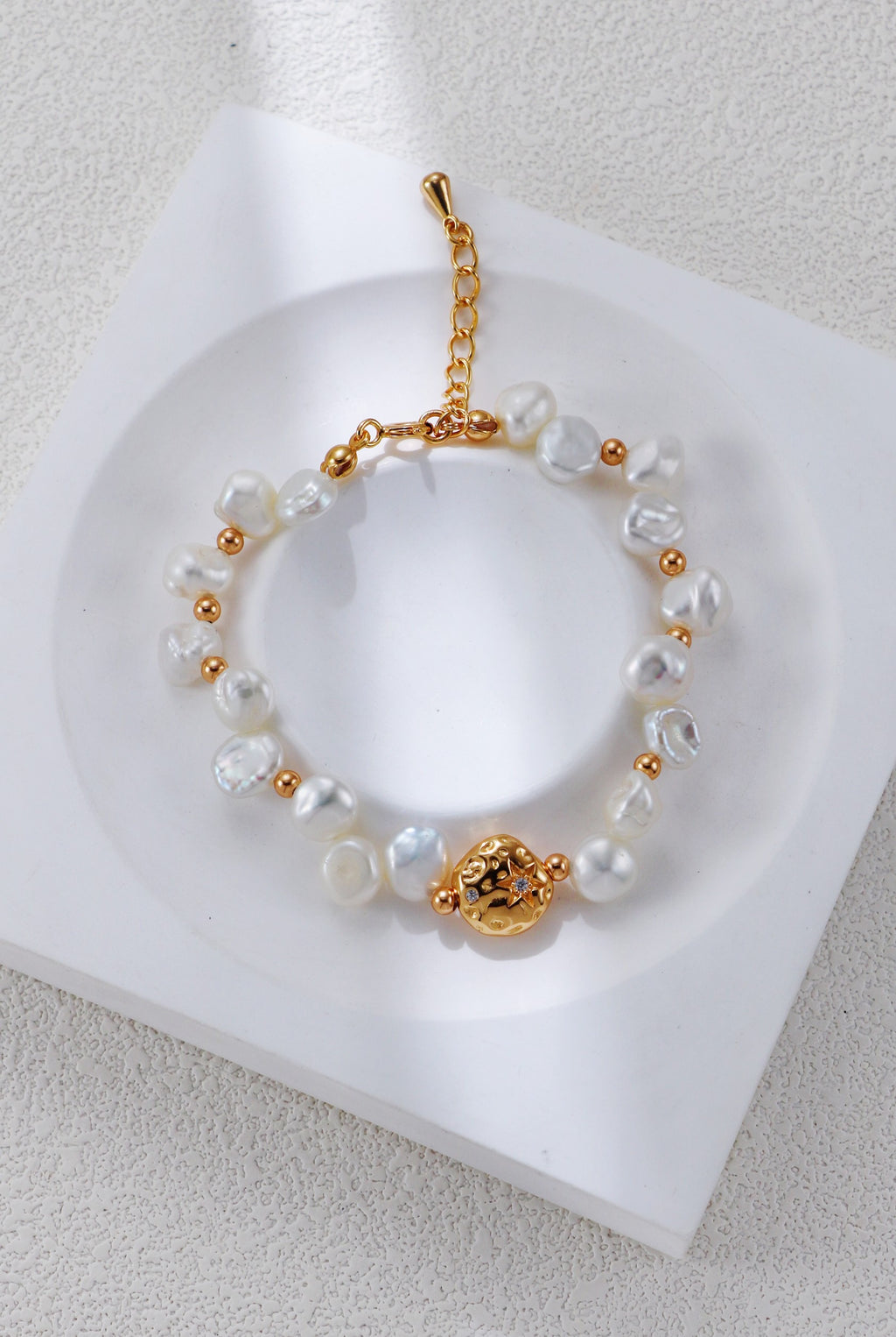 Baroque pearl bracelet in vintage gold on a white display, with round spacers and a textured centerpiece