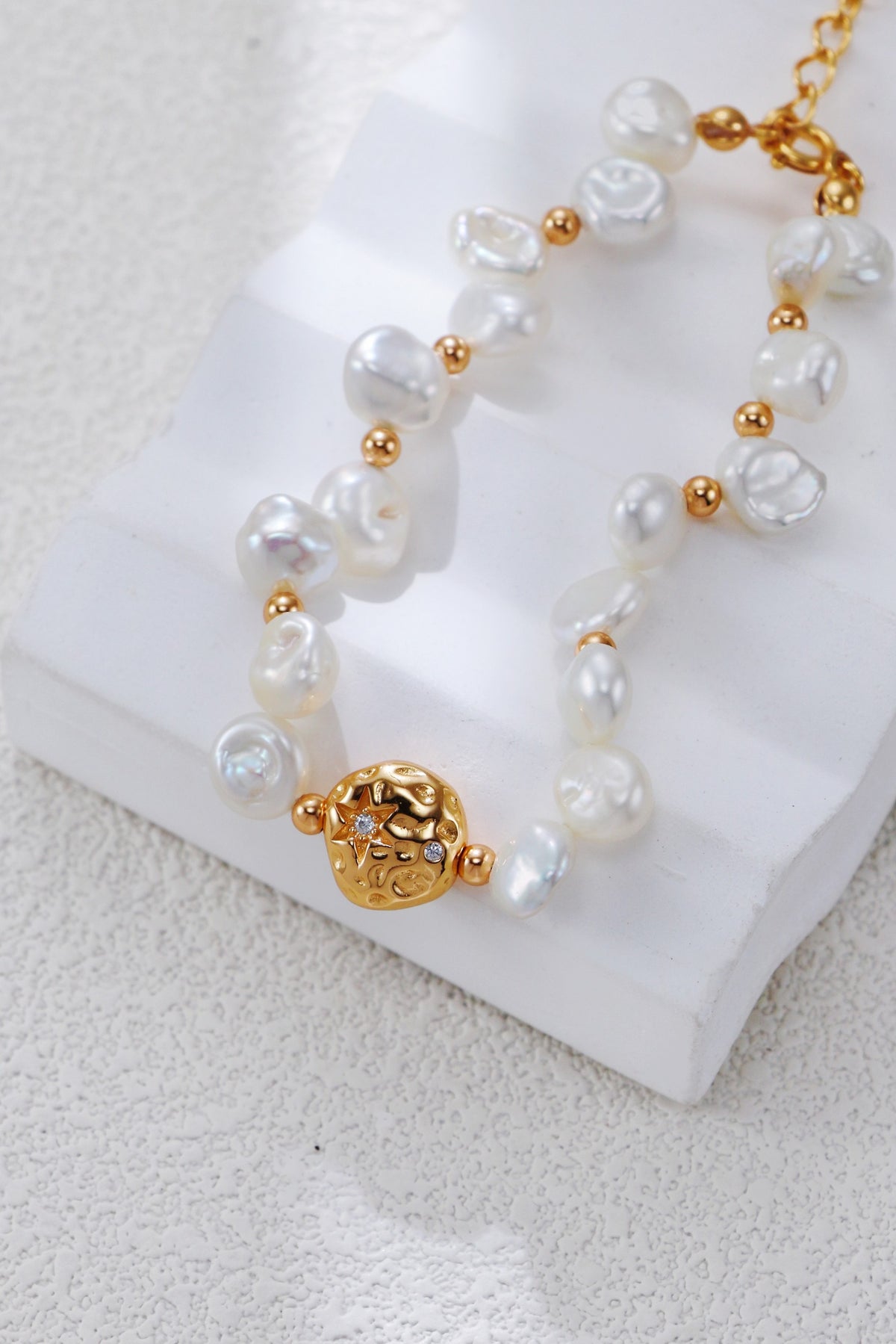 Celestial Charm pearl bracelet in vintage gold resting on a white block, with irregular pearls and round gold spacers