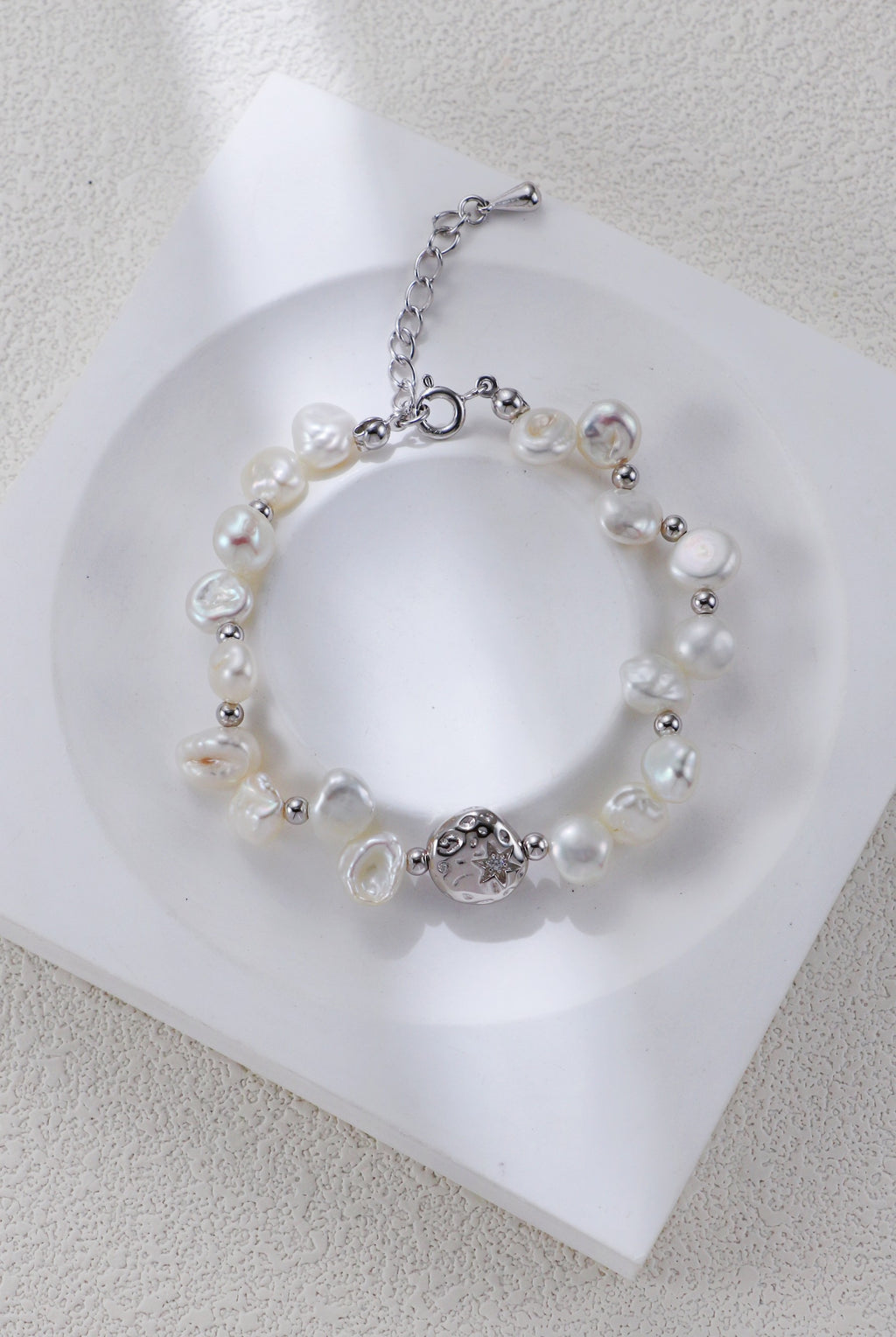 Celestial Charm pearl bracelet in platinum silver on a white display, with round spacers and a textured centerpiece