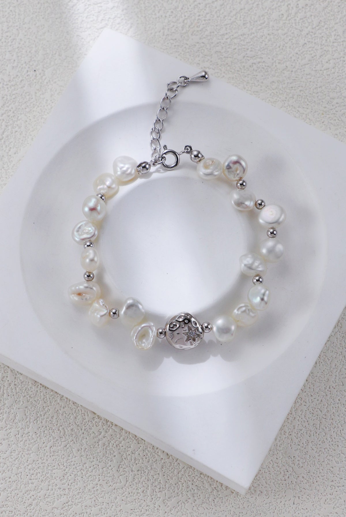 Celestial Charm pearl bracelet in platinum silver on a white display, with round spacers and a textured centerpiece