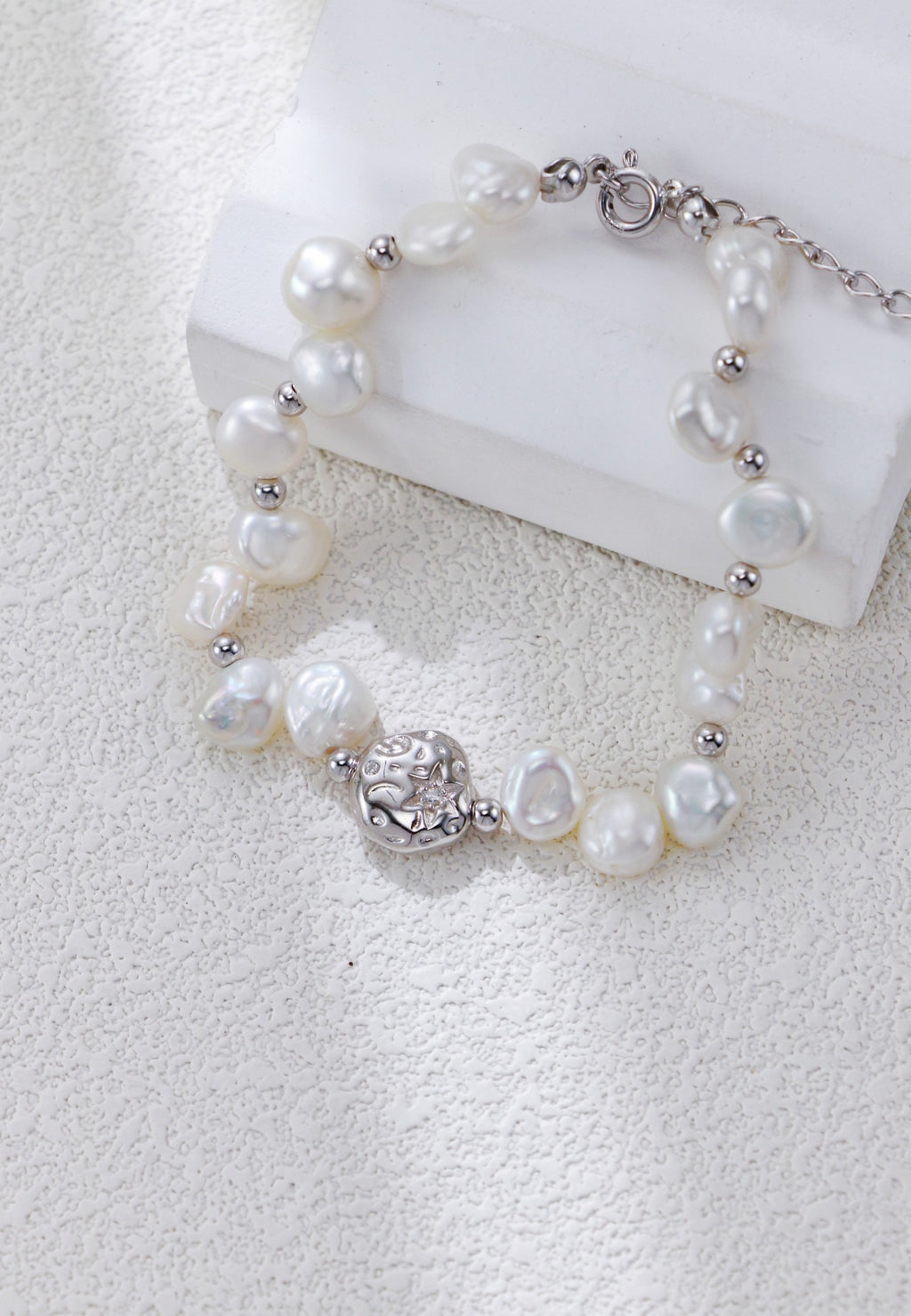 Close view of the Celestial Charm pearl bracelet in platinum silver, with irregular pearls and a textured round centerpiece