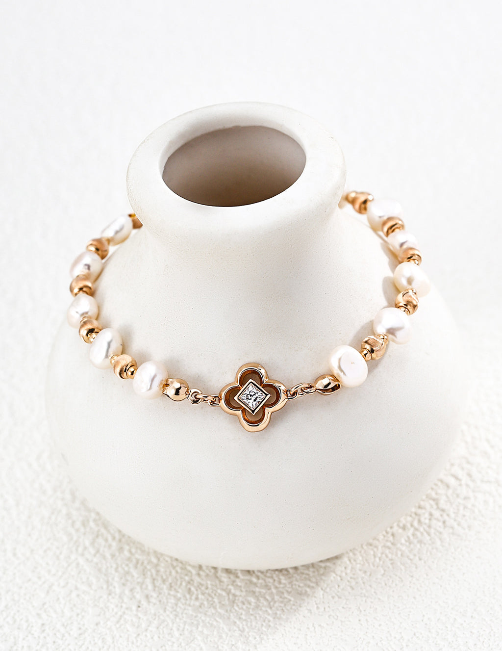 Lustrous pearl bracelet arranged around a white ceramic vase, showing vintage gold accents and a four-lobed centerpiece