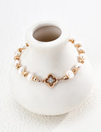 Lustrous pearl bracelet arranged around a white ceramic vase, showing vintage gold accents and a four-lobed centerpiece