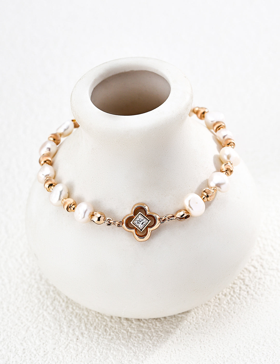 Lustrous pearl bracelet arranged around a white ceramic vase, showing vintage gold accents and a four-lobed centerpiece