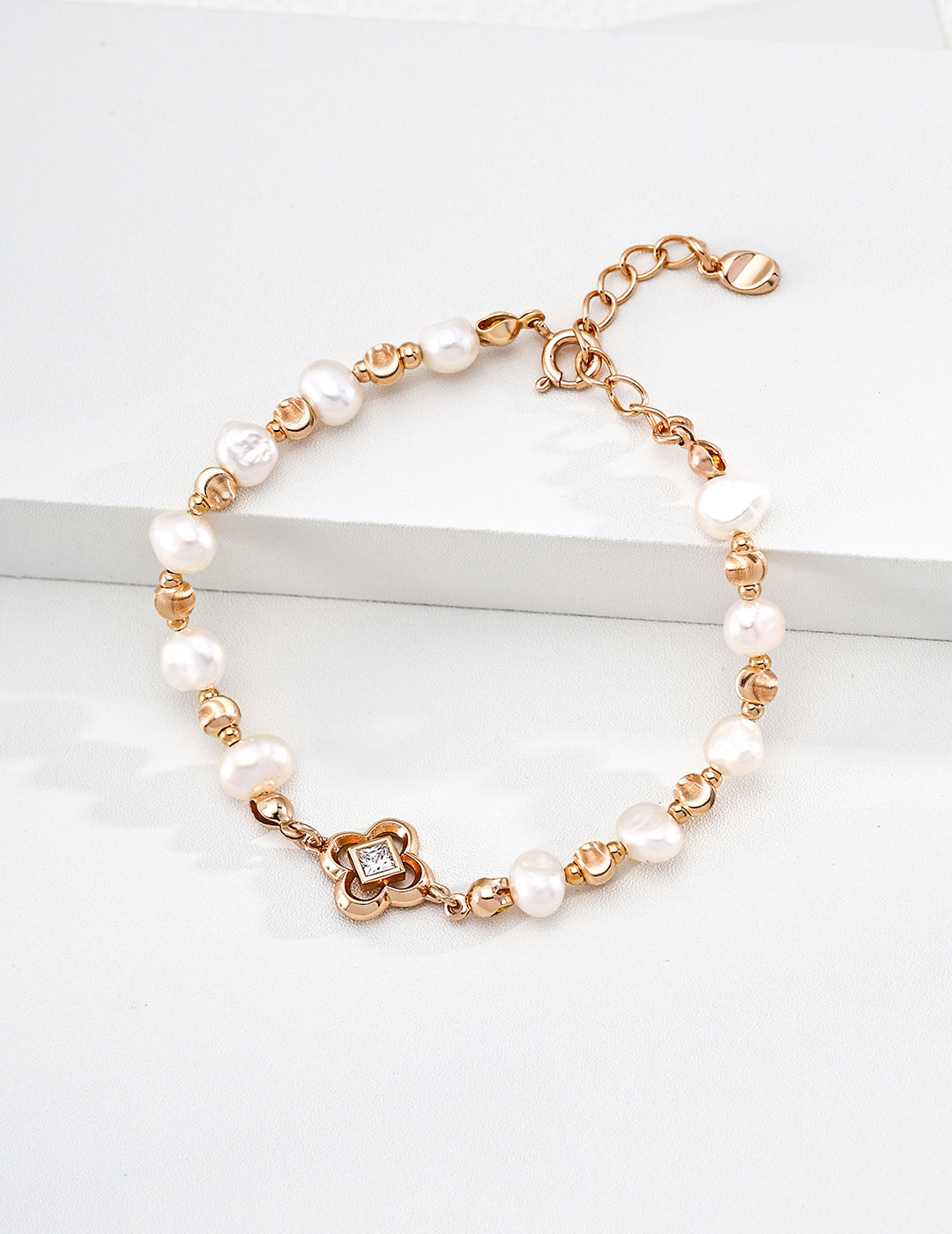 Lustrous pearl bracelet with vintage gold spacers and a four-lobed centerpiece, displayed on a white block