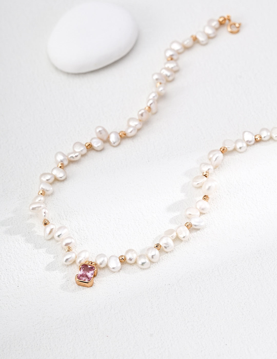 Close view of the Baroque Pearl and Pink Crystal pendant necklace, showing the pink centerpiece and vintage gold spacers