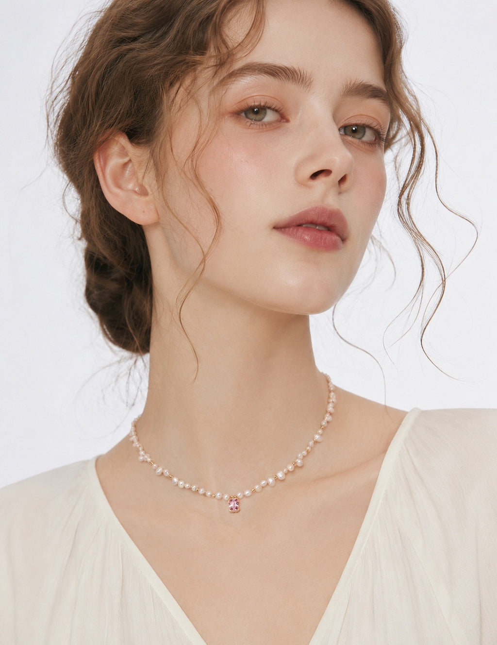 Baroque pearl necklace with a pink crystal pendant worn with a cream V-neck blouse