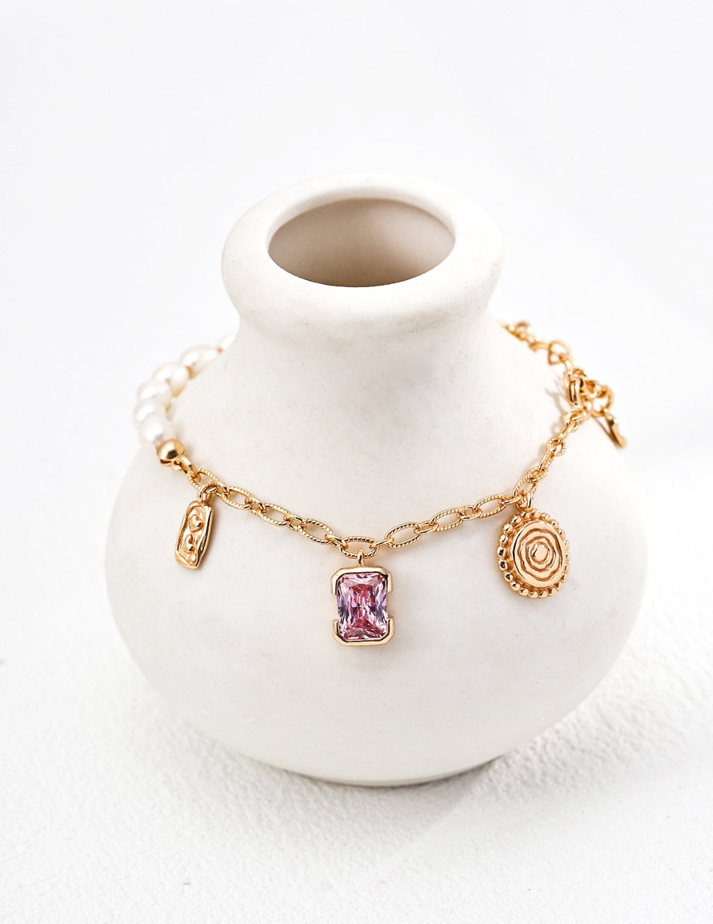 Enchanted Pink Charm pearl bracelet around a white ceramic vase, showing a pink crystal pendant and vintage gold charms
