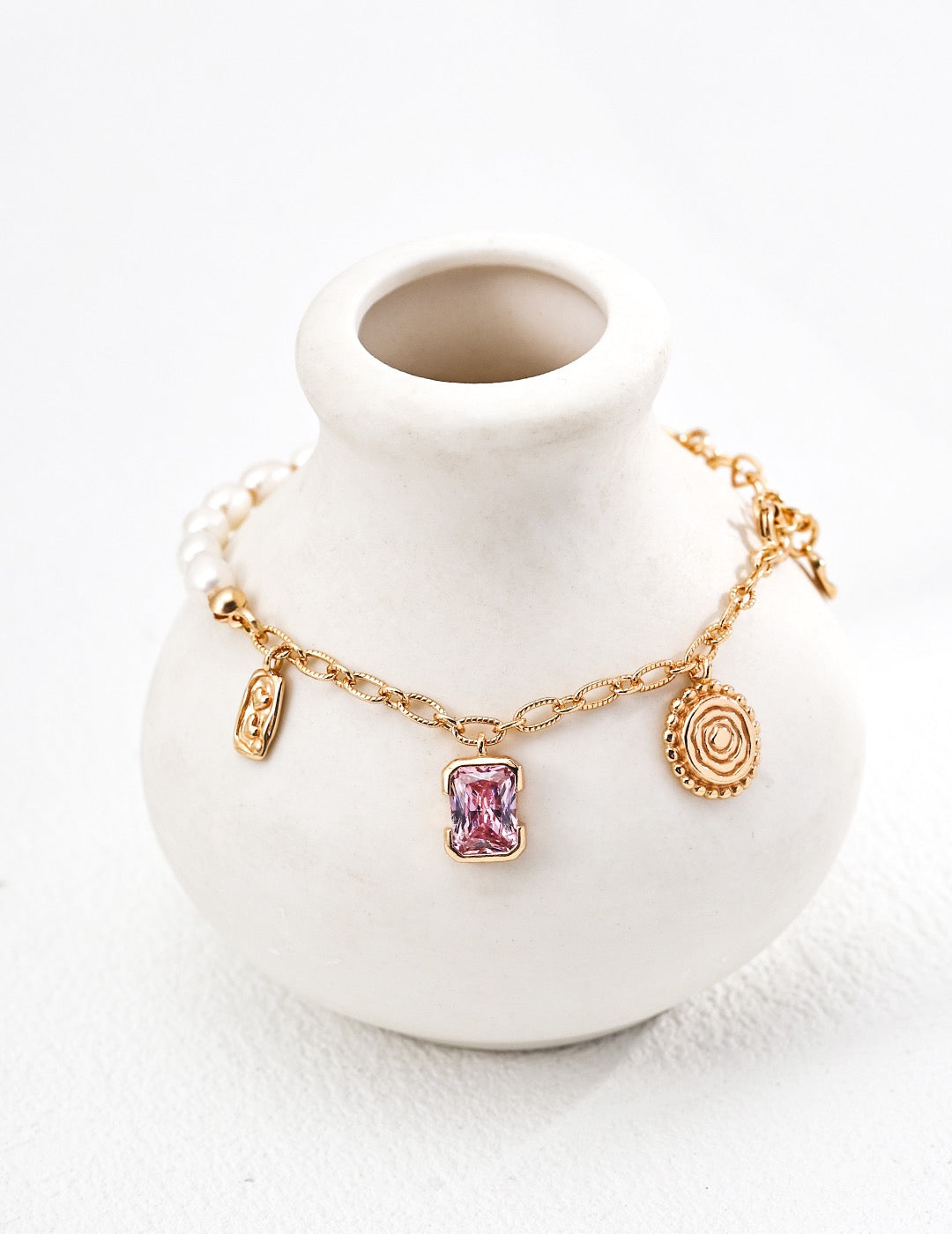 Enchanted Pink Charm pearl bracelet around a white ceramic vase, showing a pink crystal pendant and vintage gold charms